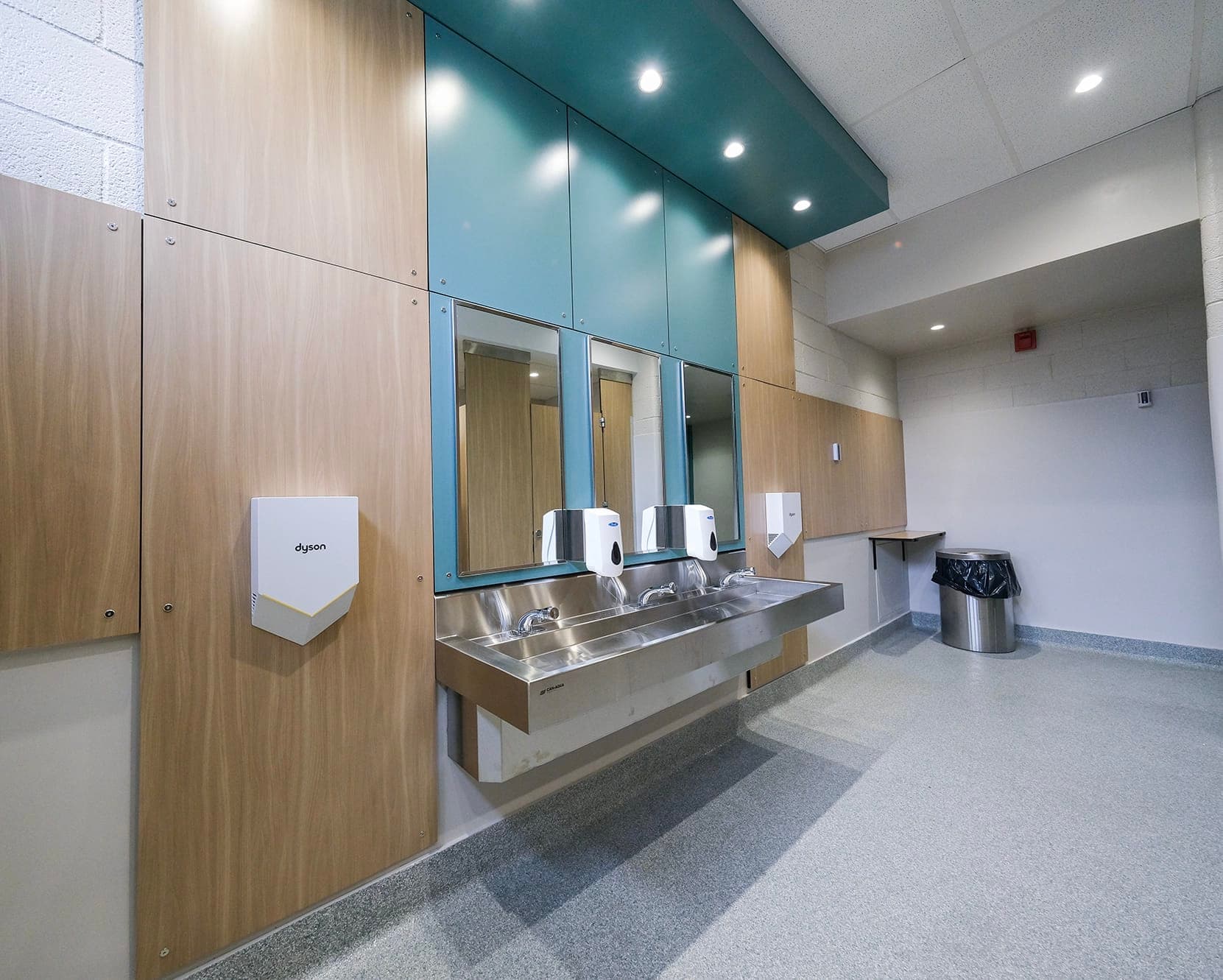 Renovated school washroom with stainless-steel sinks and wood panels