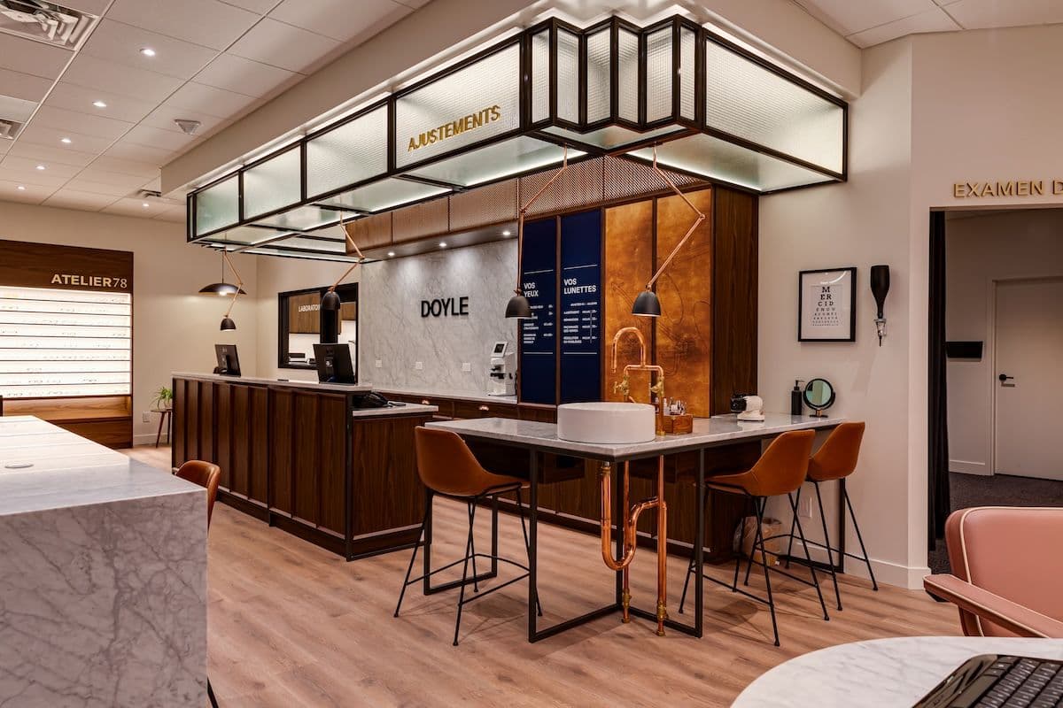 Intérieur de la lunetterie Doyle à Joliette : comptoir d’accueil, îlot d’ajustement en acier et cuivre, sièges en cuir