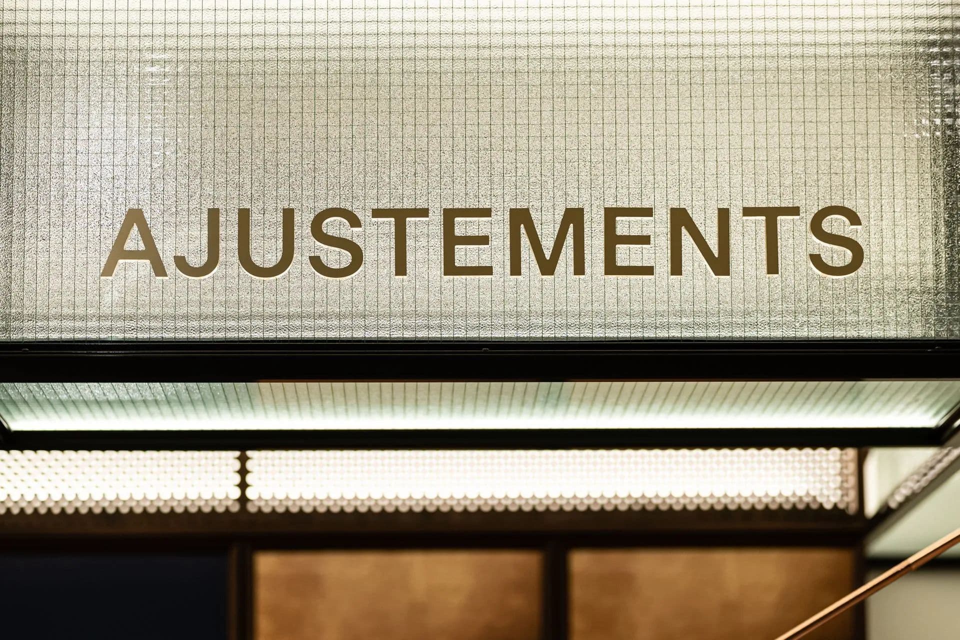 Enseigne « Ajustements » en lettres dorées sur verre texturé