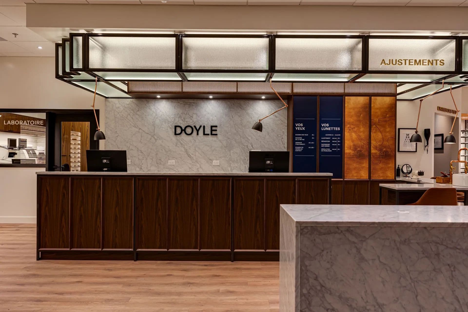 Comptoir d’accueil en bois foncé, îlot en marbre et enseignes Laboratoire et Ajustements