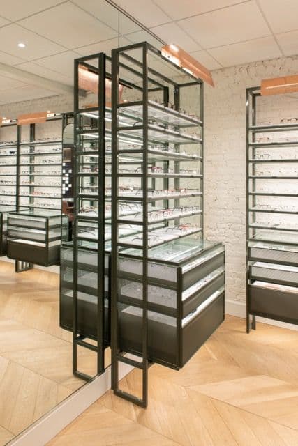Vitrine-présentoir en acier et verre devant un mur de brique peint en blanc