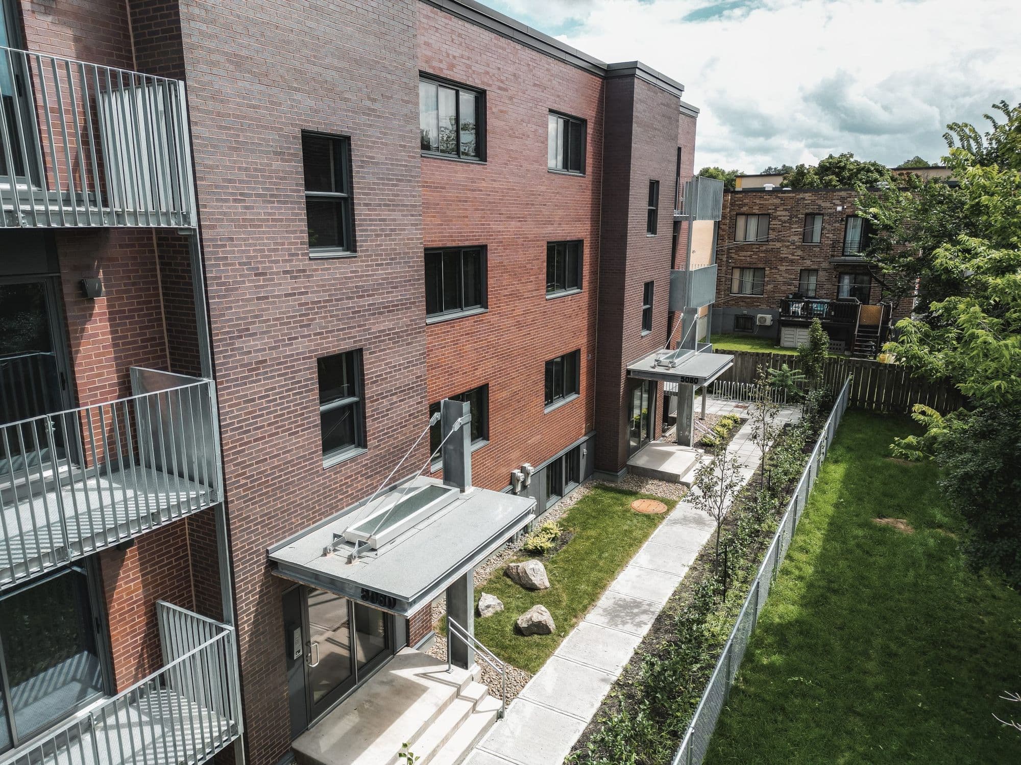 Façade arrière en brique avec balcons en acier galvanisé et cour gazonnée