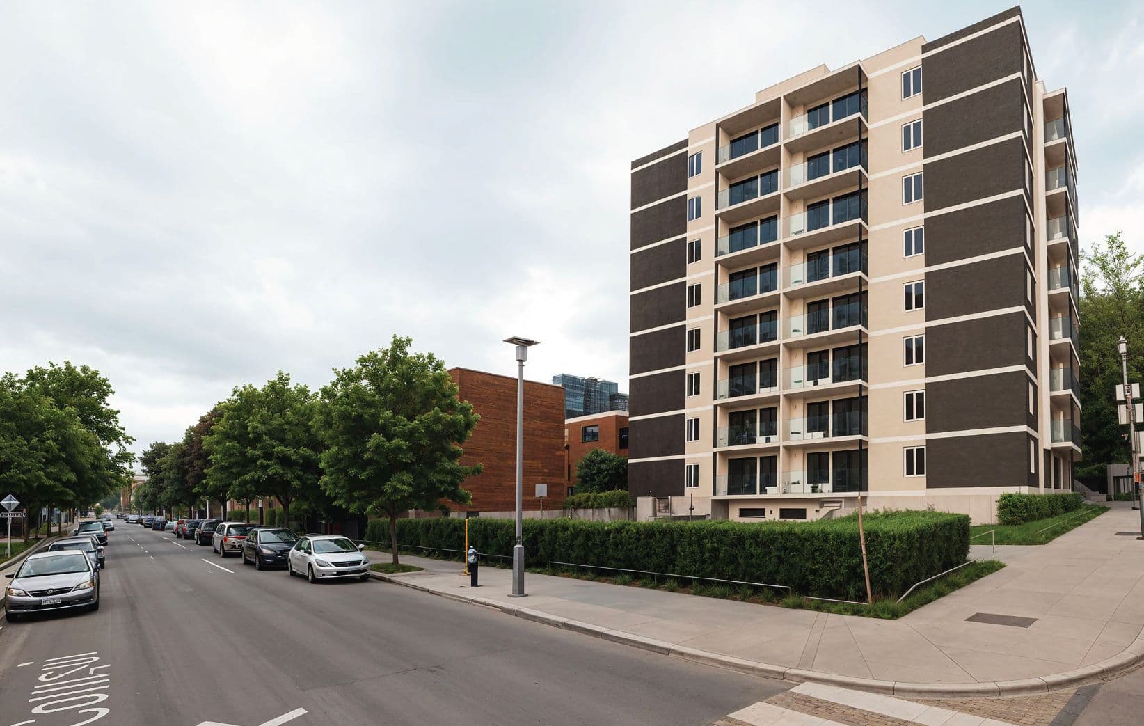 Immeuble d’habitation de huit étages aux balcons en retrait, vu depuis une rue résidentielle