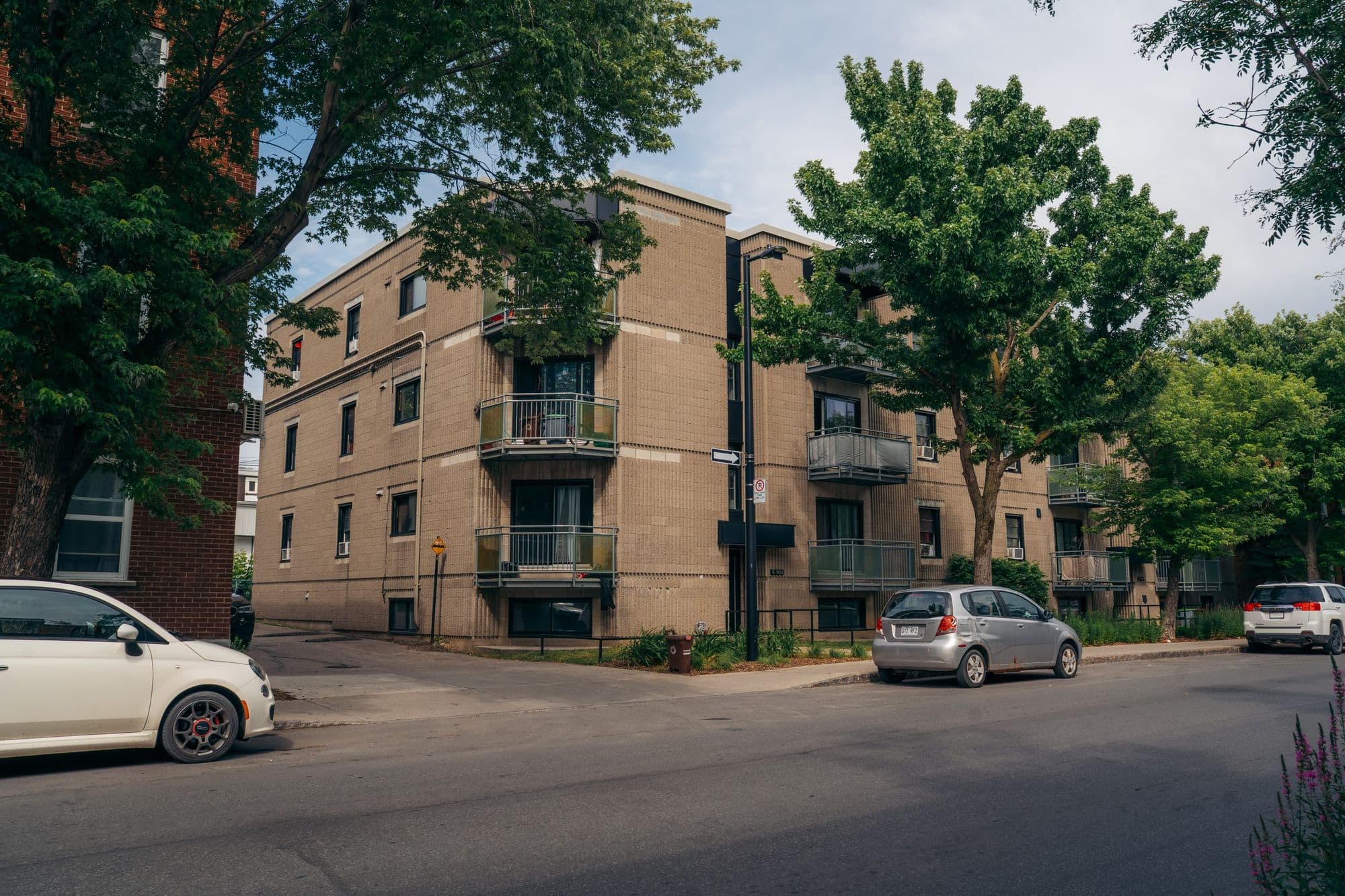 Immeuble de trois étages en brique beige avec balcons, vu depuis l’angle de la rue