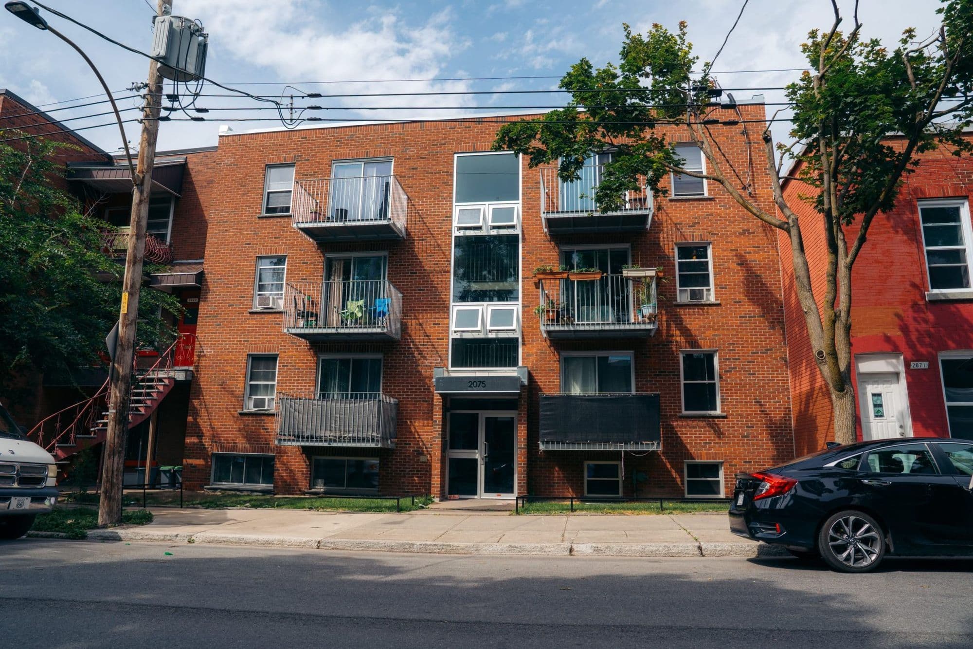 Immeuble de trois étages en brique rouge avec balcons, vu de la rue